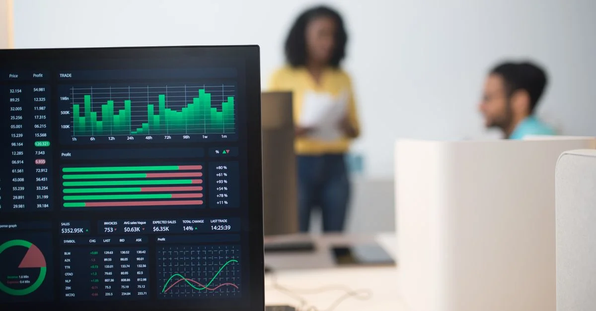 Bureau moderne avec des écrans de trading financier et une équipe diversifiée discutant des stratégies.